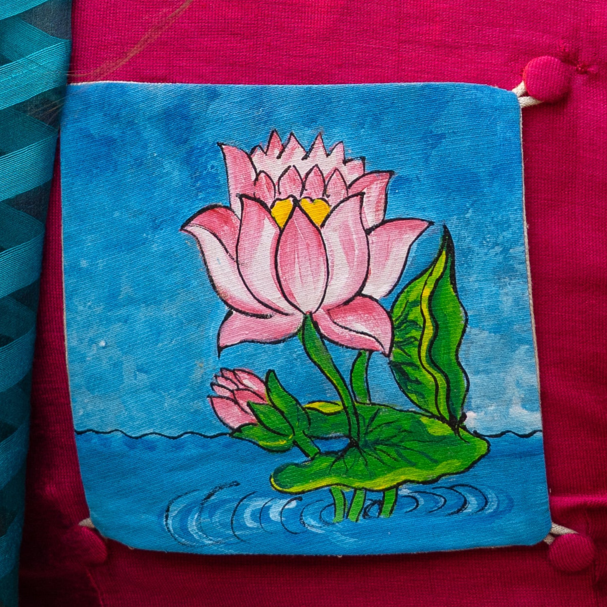 Woman wearing a pink blouse with a floral design and a blue saree, standing against a green leafy background.